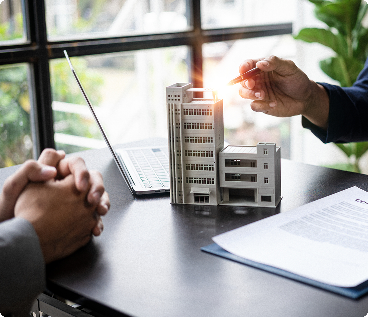Hands discussing model building and contract document.